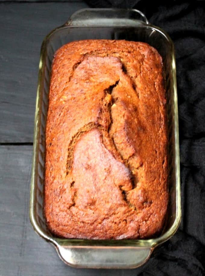 Front shot of a full loaf of rich brown banana bread in a glass loaf pan on a gray background