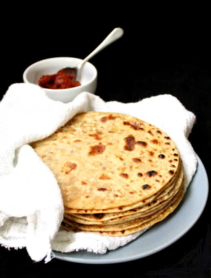 Tofu Paratha in gray plate wrapped in napkin with tomato chutney in bowl behind.