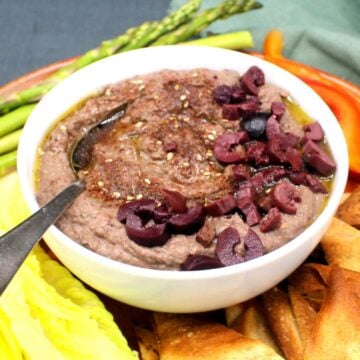 Black bean hummus in bowl surrounded by pita wedges and vegetable crudites.