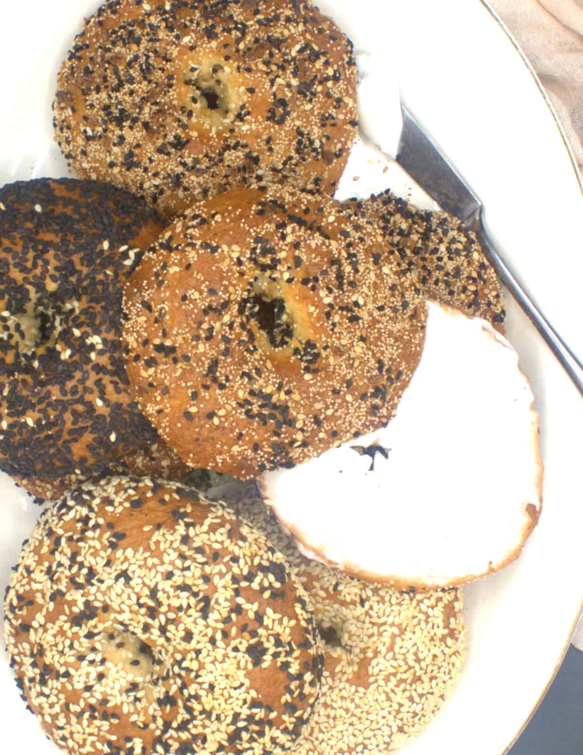 Vegan bagels on platter, one open with a schmear of vegan cream cheese.