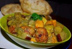 Oondhiyu, a Gujarati vegetable curry with dumplings, in a green bowl with pooris