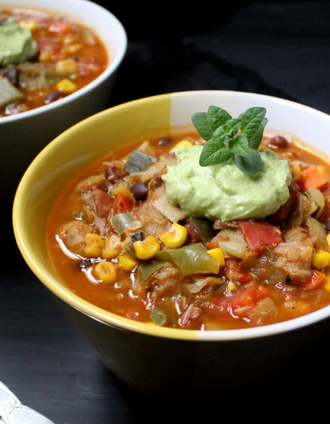 Vegan chili topped with avocado crema in bowls with mint garnish.