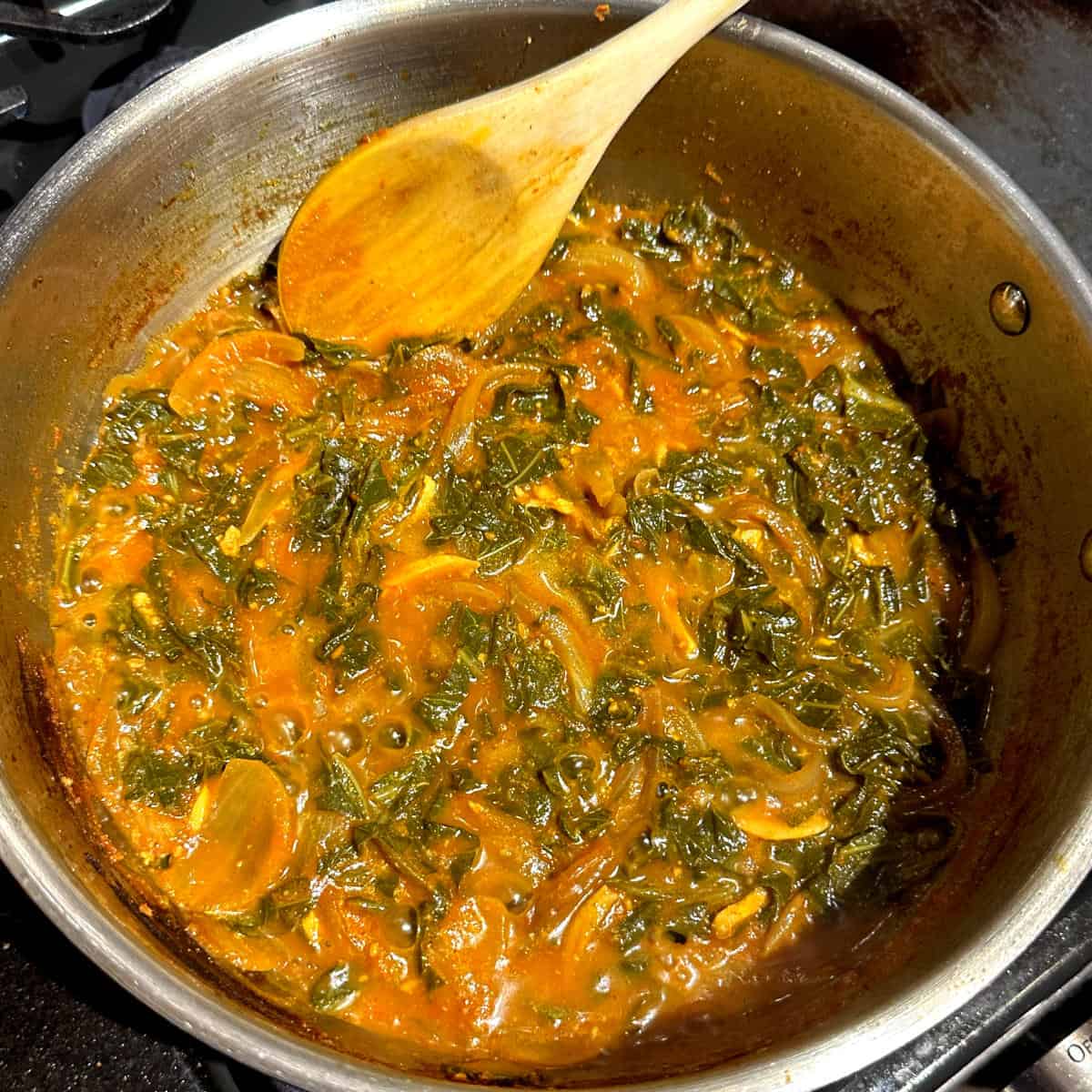 Kashmiri collard greens, cooked, in pan with wooden ladle.