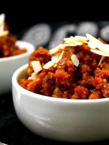Partial shot of a bowl filled with gajar ka halwa and sliced almonds