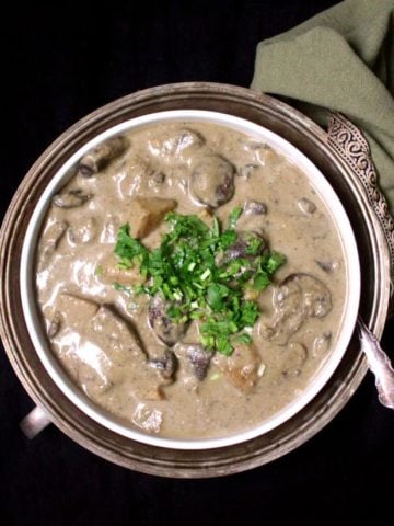 Malaysian mushroom korma in white bowl with cilantro garnish and spoon.