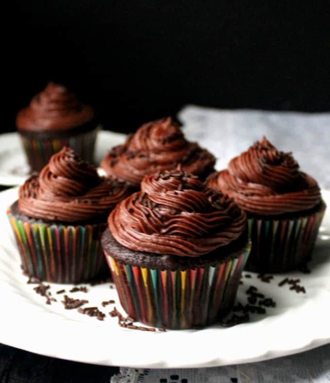 Four vegan chocolate cupcakes with mounds of vegan chocolate buttercream frosting on a white plate,