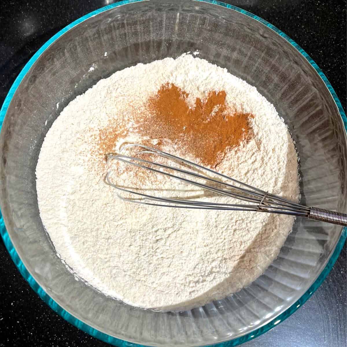 Cinnamon added to flour and baking soda and baking powder in bowl with whisk.