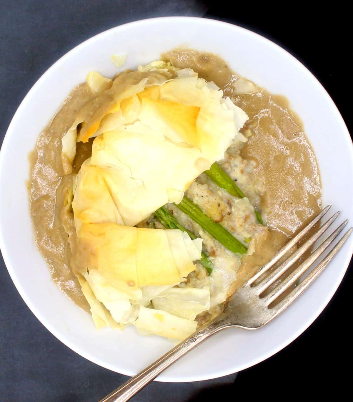 Vegan asparagus potato tart with vegan gravy in a bowl with fork.