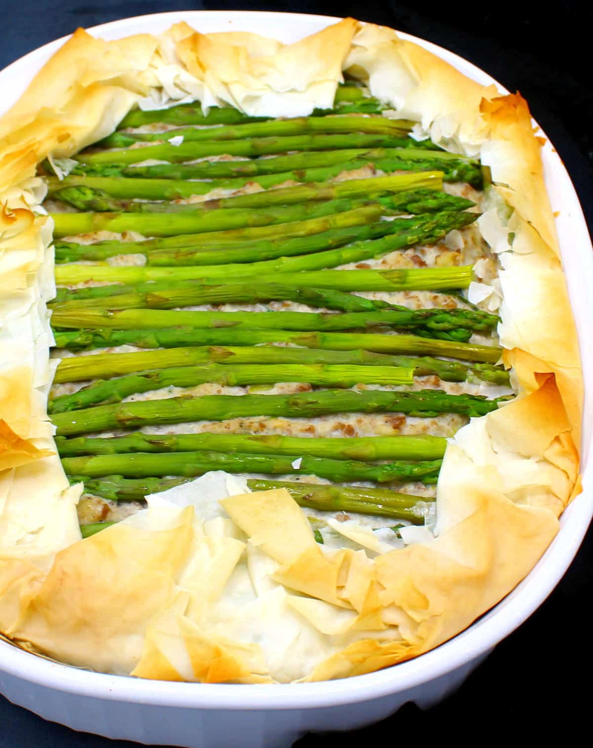 Baked vegan asparagus tart with golden edges in baking dish.