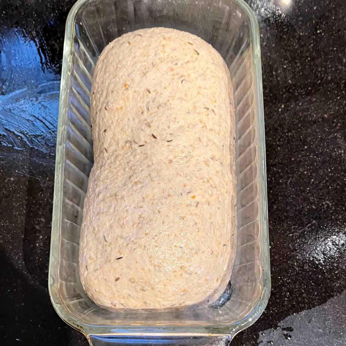 Shaped rye bread loaf placed in glass loaf pan.