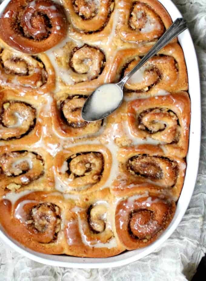 A white baking dish with vegan cinnamon rolls packed in it and drizzled with a vanilla cashew glaze