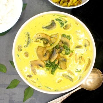 Bright yellow vegan mushroom curry in a white bowl with spoons on the side.