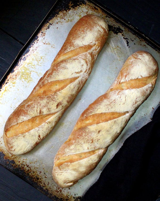 Bakery style French bread loaves on baking sheet lined with parchment paper.
