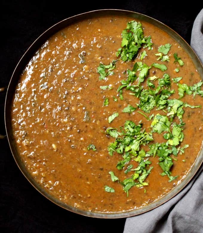 A copper pan with spicy urad dal with cilantro garnish.