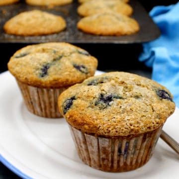 Vegan Blueberry Muffins in a white and blue plate with a muffin pan in the background
