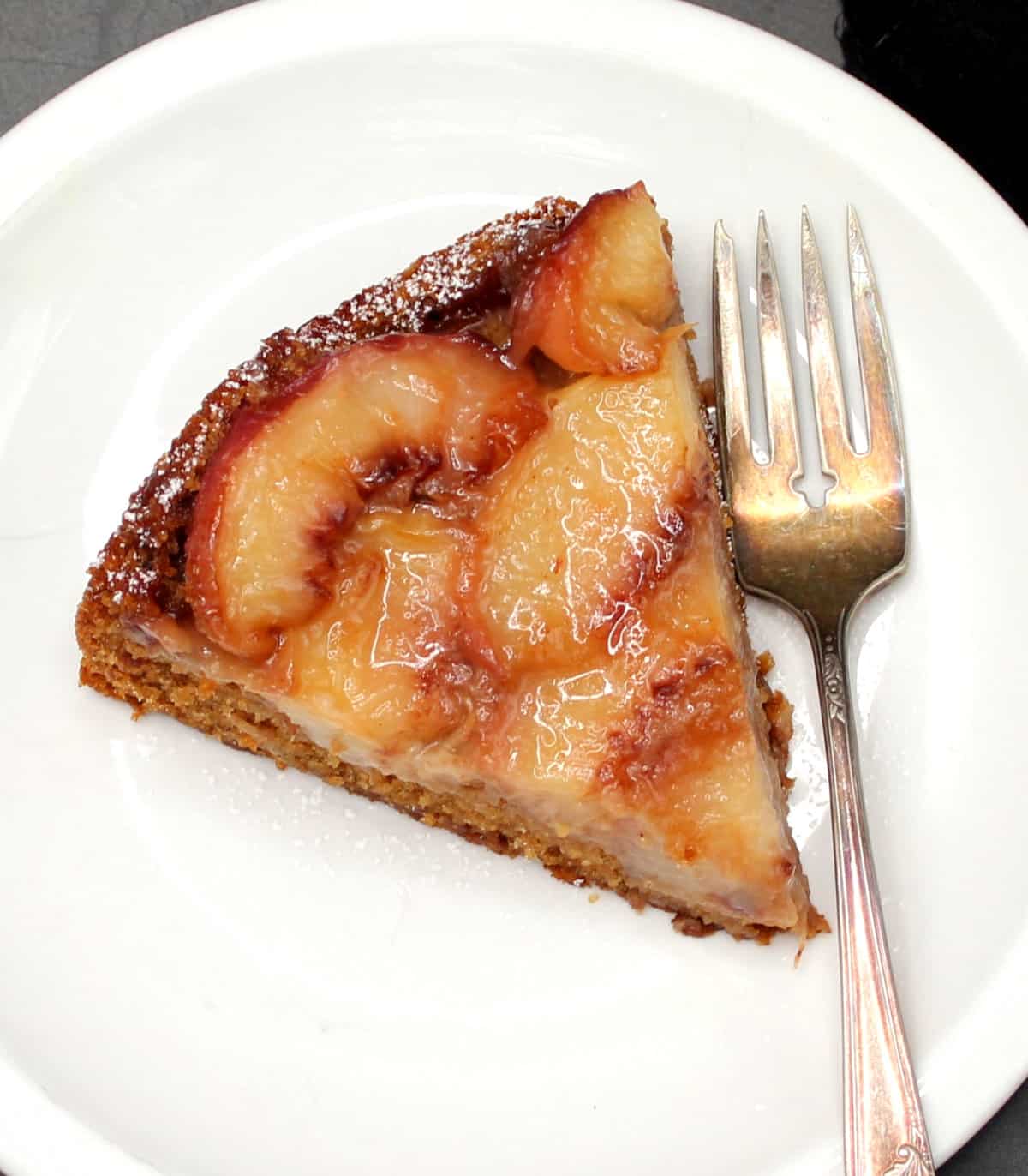 A slice of vegan peach upside-down cake on white plate with fork.