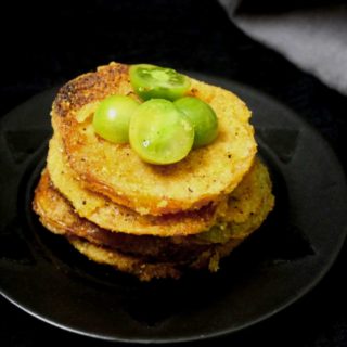 A black plate with slices of vegan fried green tomatoes stacked over it and a gray napkin in the background