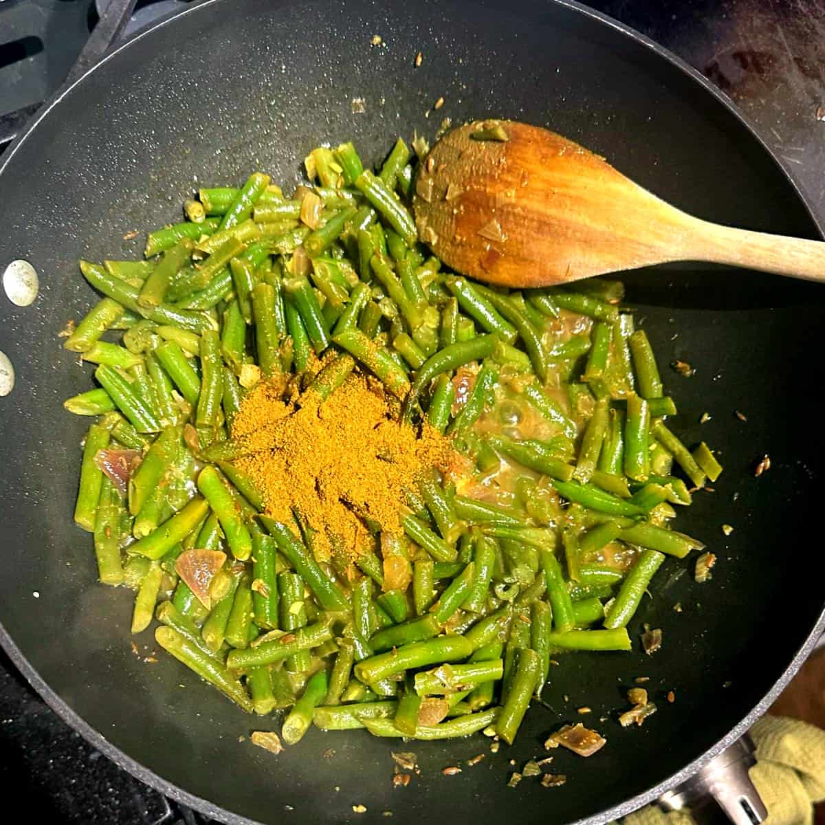 Curry powder added to Trinidadian green beans in wok.
