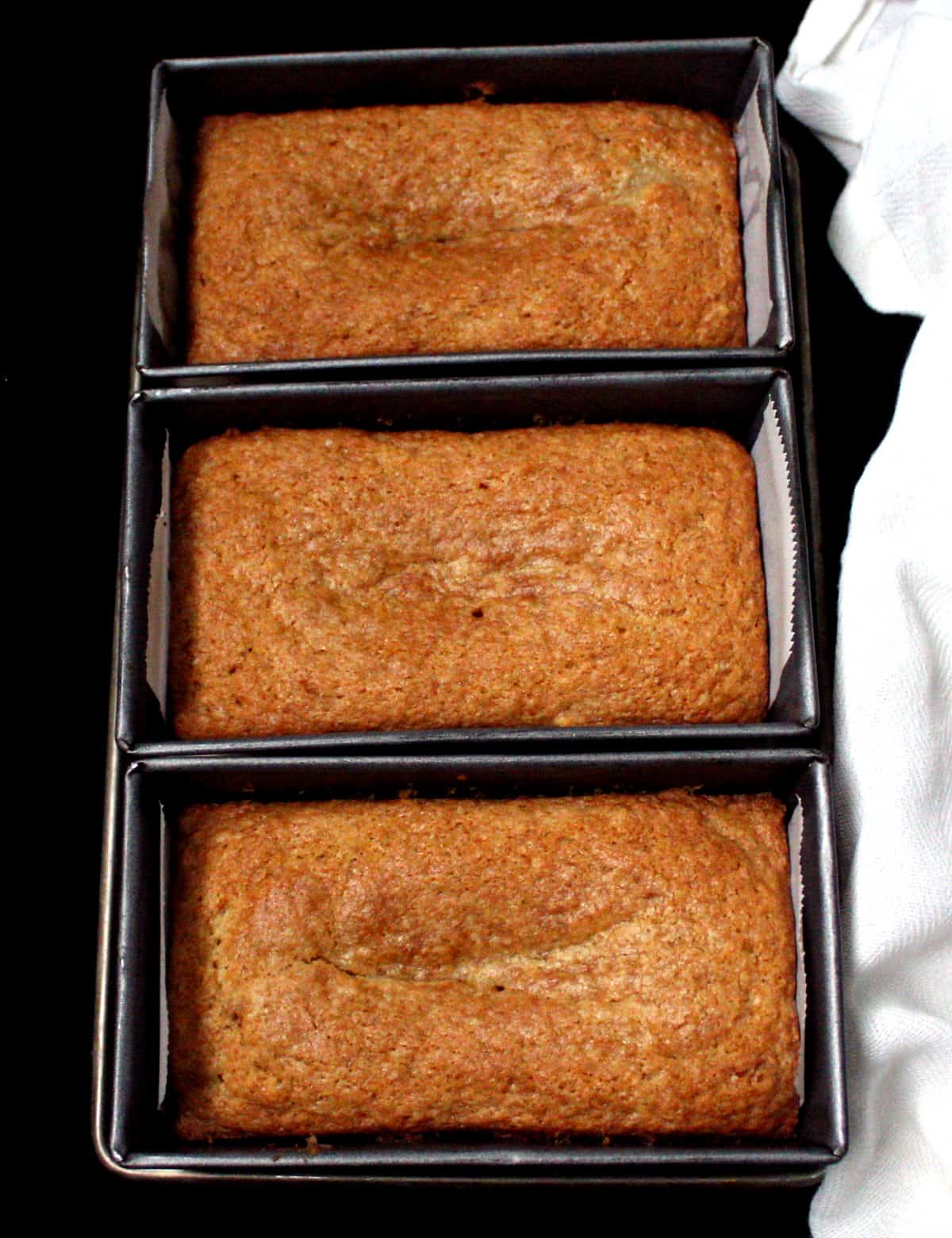 Three loaves of vegan mawa cake in min loaf pans with a white napkin