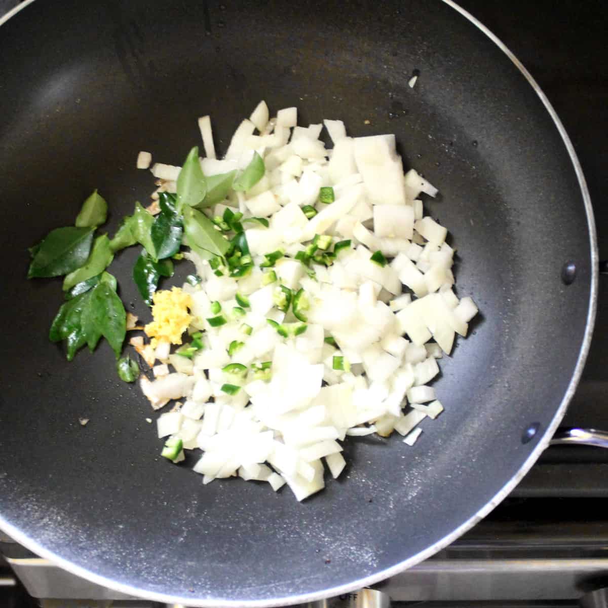 Onions, curry leaves, cilantro and green chili peppers in a wok