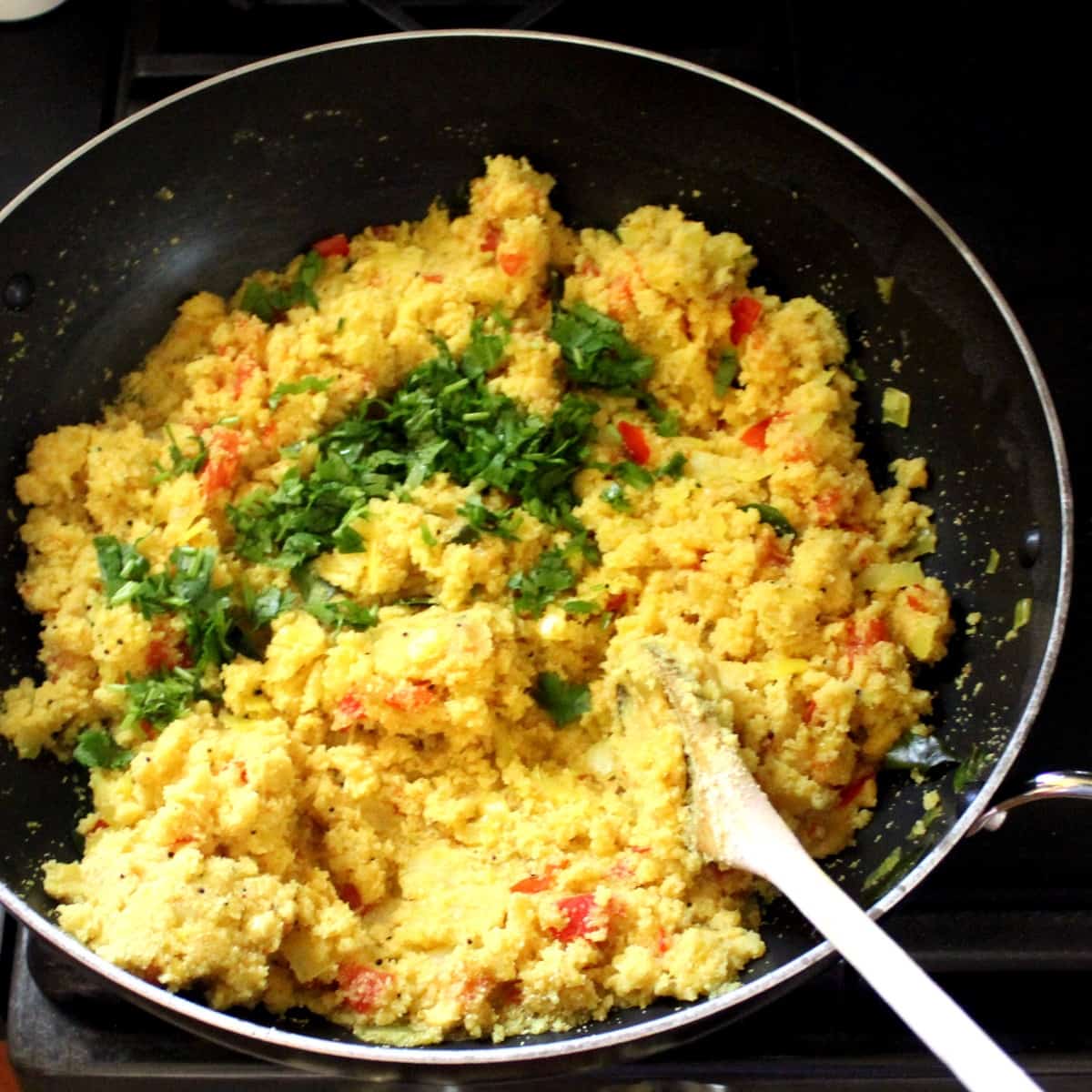 A photo of fluffy rava upma freshly made and garnished with cilantro in a wok with a wooden ladle