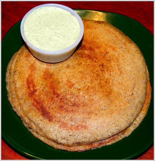 Brown rice dosas stacked on a green plate with coconut chutney in a bowl.