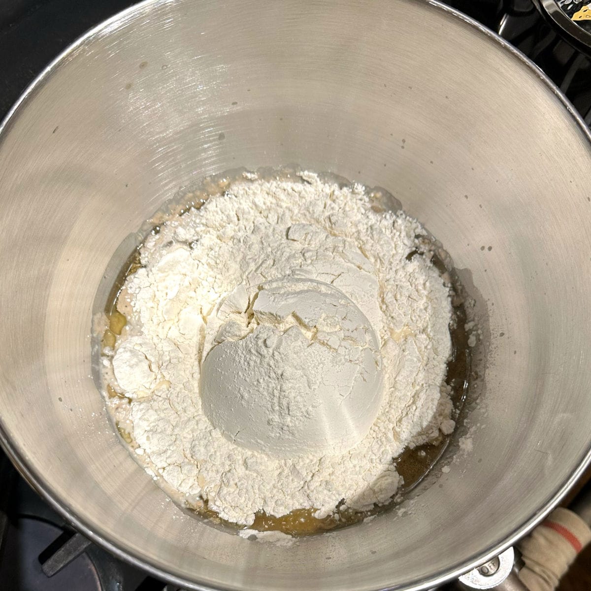 Bread flour added to yeast and milk in bowl.