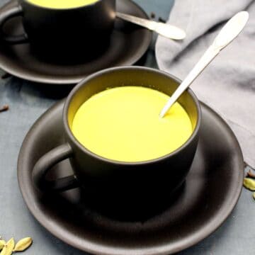 Turmeric latte in a cup and saucer with spoon. Spices are strewn around.