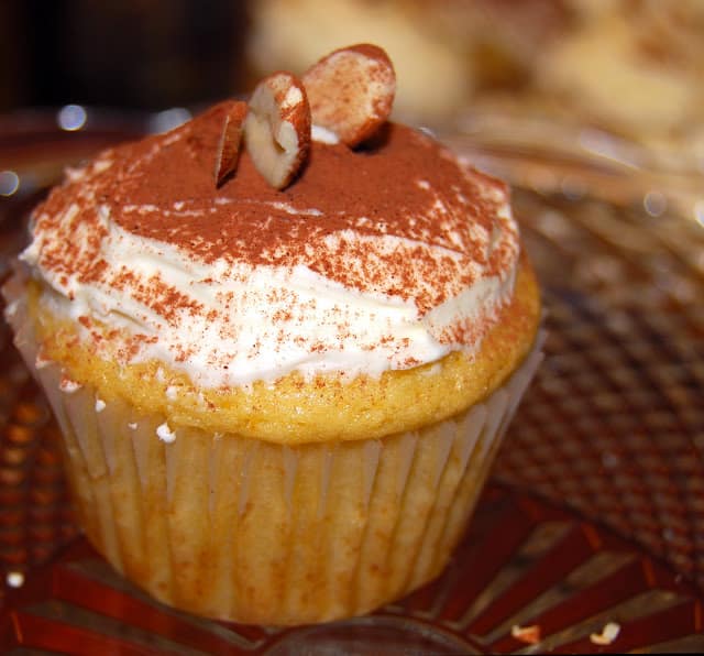 A vegan orange cupcake with orange buttercream frosting decorated with almonds with a shower of cocoa.