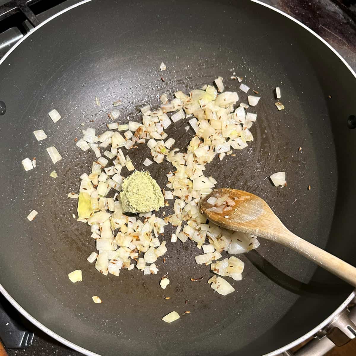 Ginger garlic paste added to onions in wok.,