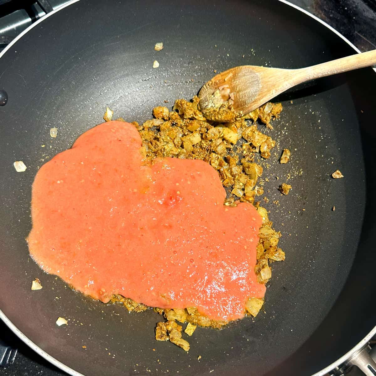 Tomato puree added to wok with onions and spices.