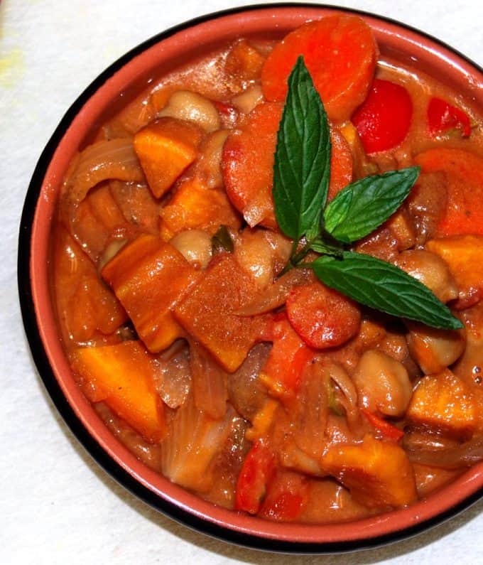 African Peanut Sweet Potato Stew in an earthenware bowl with a black rim on a white tablecloth.