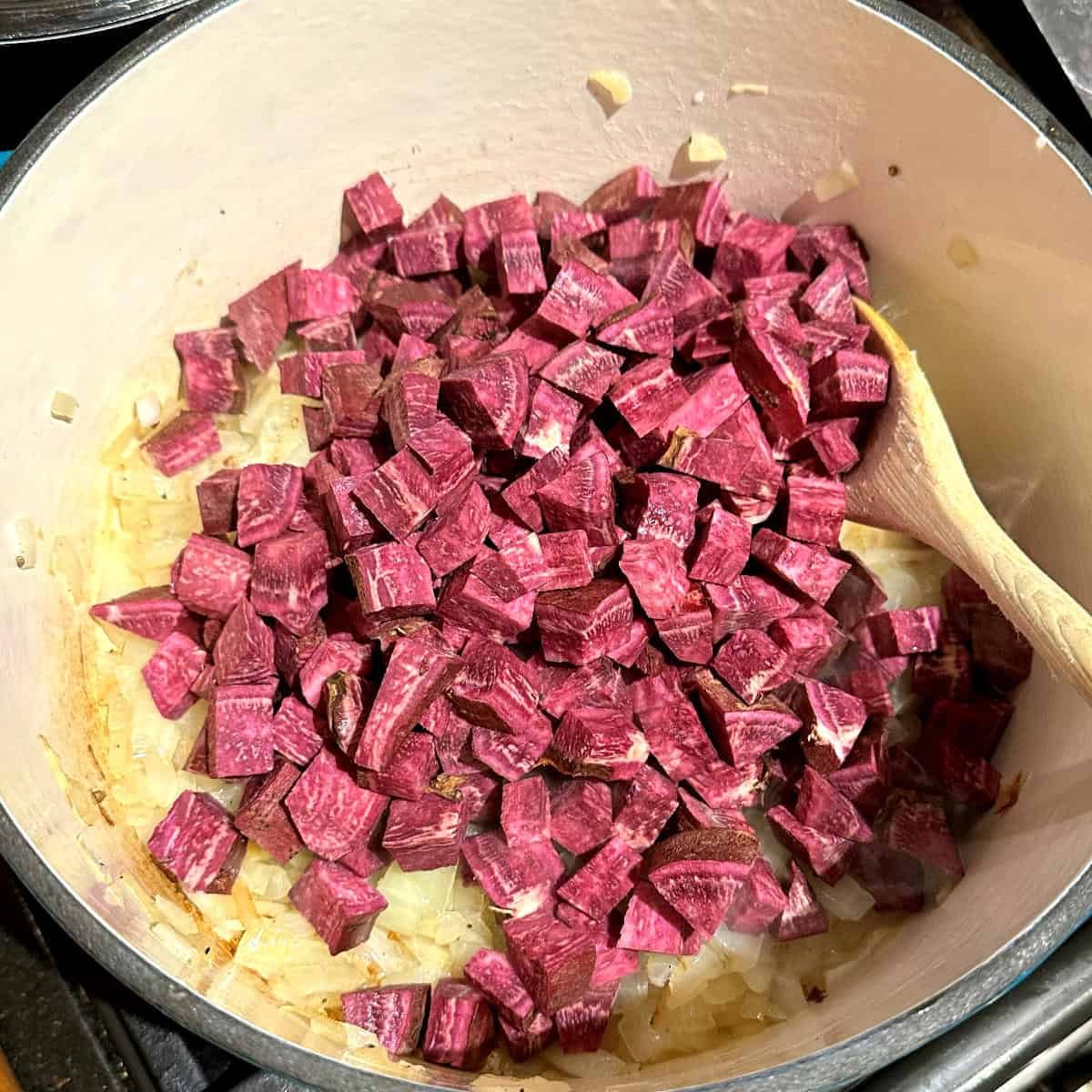Purple sweet potatoes added to dutch oven with onions.