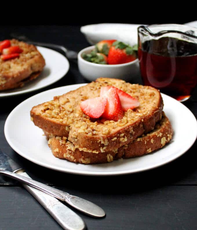 A front shot of a plate of vegan French toast with fresh strawberries and maple syrup.