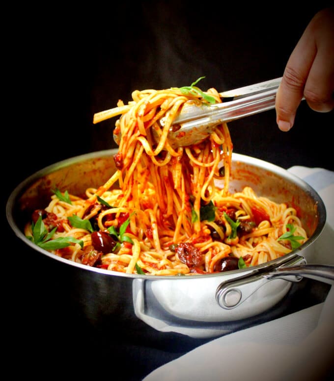 Vegan Pasta Puttanesca being served with tongs.