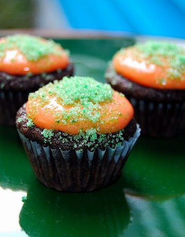 Vegan cupcakes with orange icing and green colored sugar topping on a green plate.