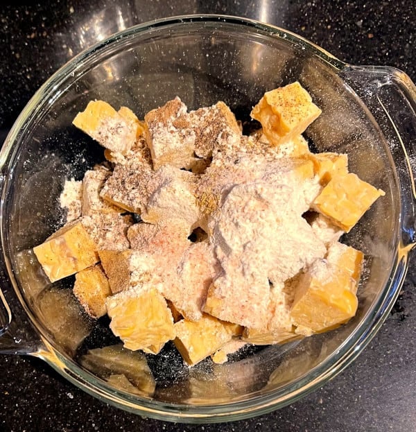 Tempeh cubes in bowl with flour, herbs, salt and pepper