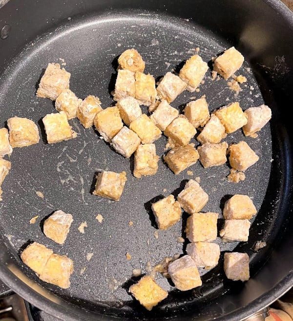 Tempeh cubes with flour, herbs and spices added to sautee pan.