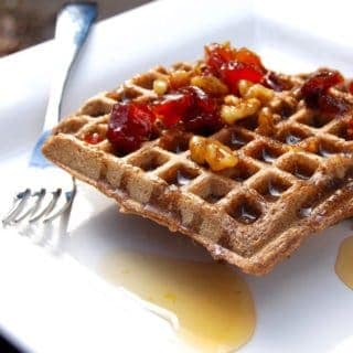 Vegan buckwheat waffles with glazed apricots and maple syrup on white plate with fork.