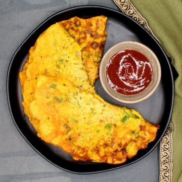 Besan chilla on black plate with red sauce.