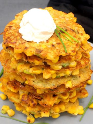 A stack of vegan corn fritters with chives and cream cheese on a gray plate