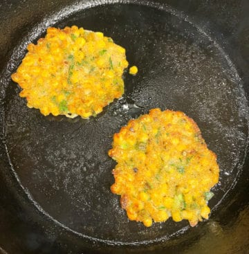 Vegan corn fritters frying on a cast iron skillet.