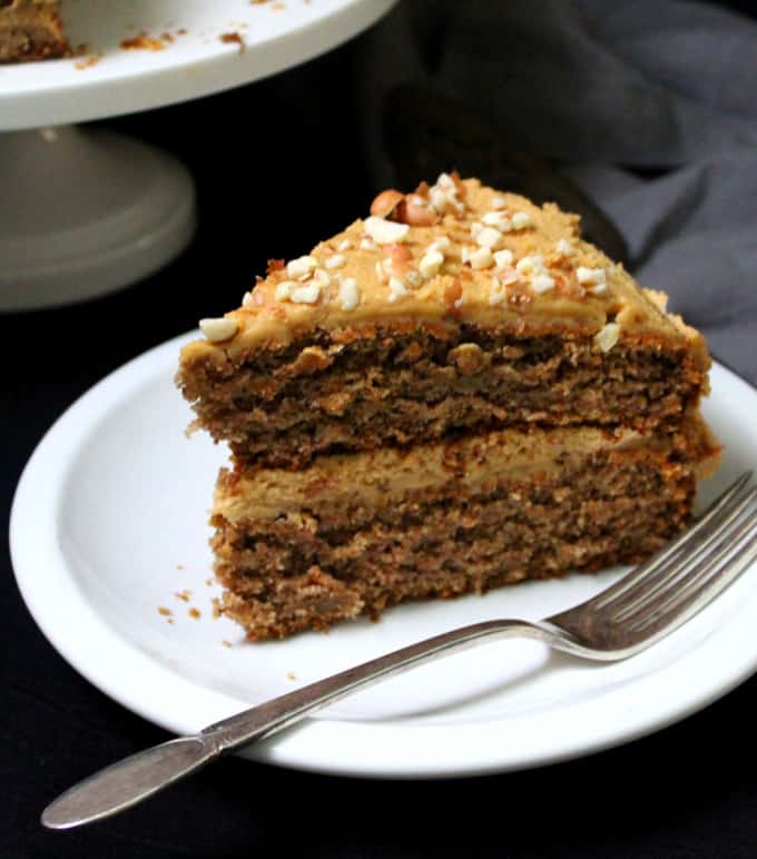 A big slice of vegan banana cake with peanut butter frosting on white plate wiht fork.