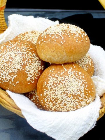 Whole wheat hamburger buns in a straw basket nestled in cheesecloth