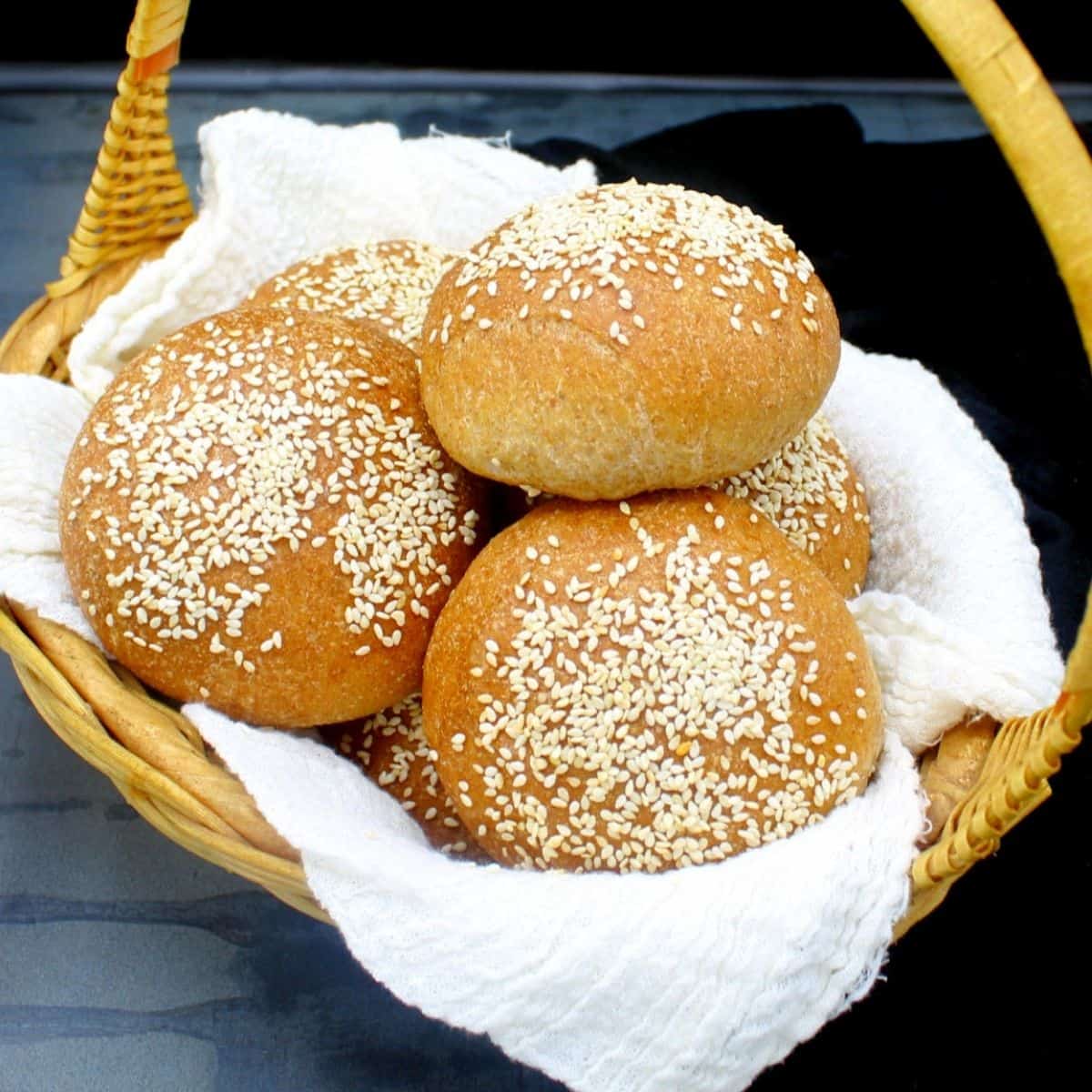 Whole wheat hamburger buns in a straw basket nestled in cheesecloth
