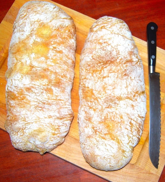 Two perfect ciabatta bread loaves on a chopping board witha  knife.
