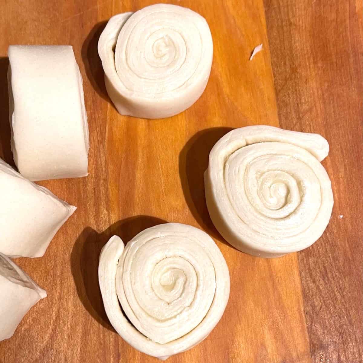 Cut outs of coiled dough on wooden board.