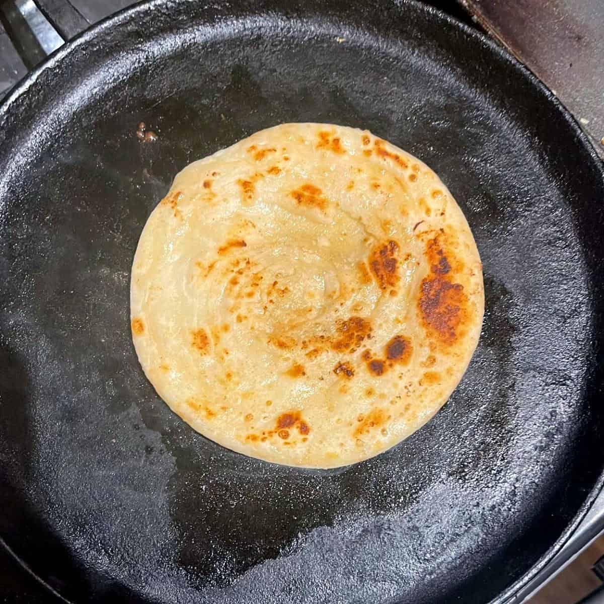 Paratha roasted to golden-brown perfection on cast iron griddle.