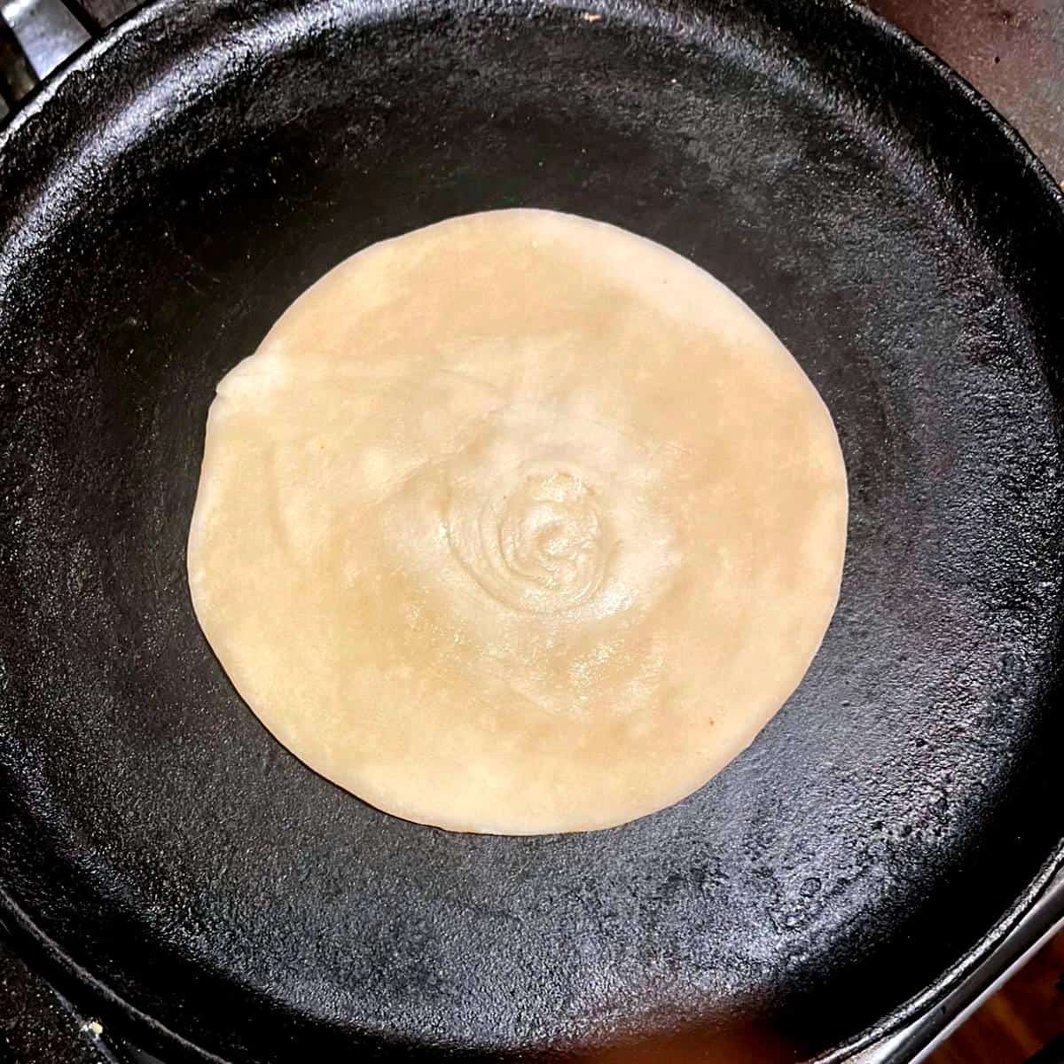 Paratha placed on griddle for roasting.