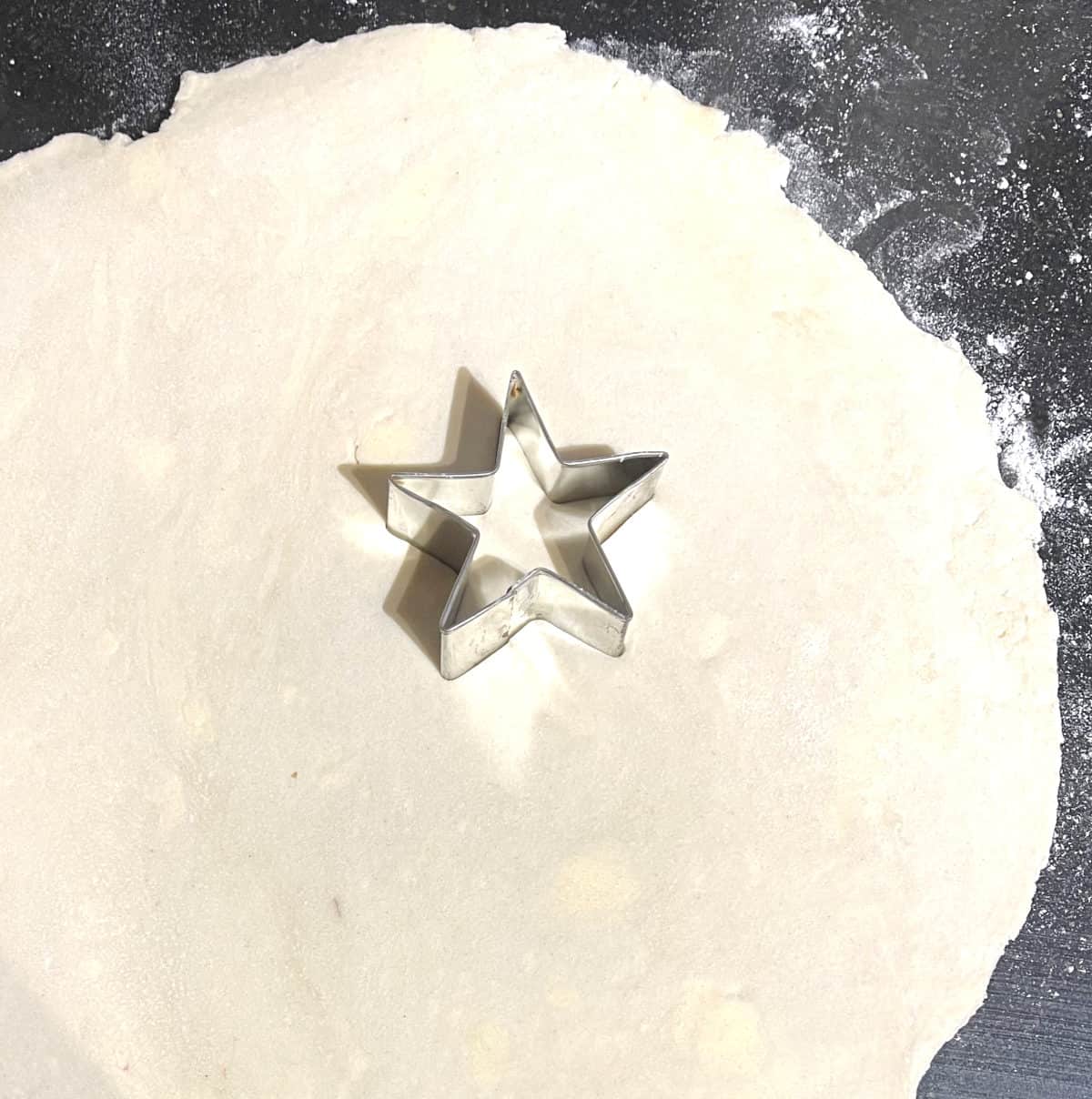 Star cookie cutter on rolled out pie dough.
